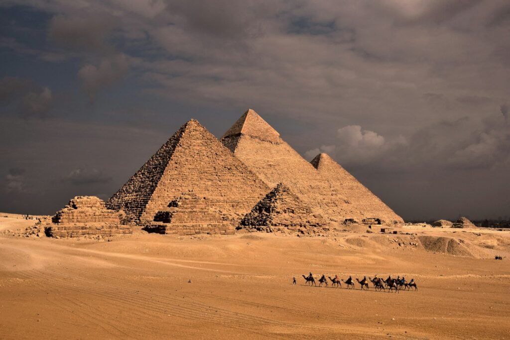 a group of people riding camels in front of three pyramids