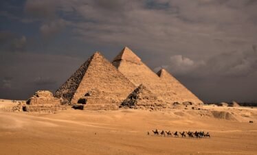 a group of people riding camels in front of three pyramids