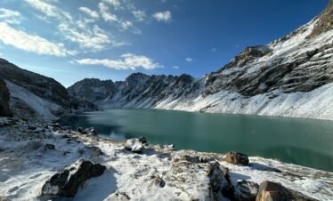 a lake surrounded by snow covered mountains under a blue sky