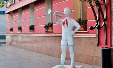Statue of a boy playing a trumpet on a sidewalk.